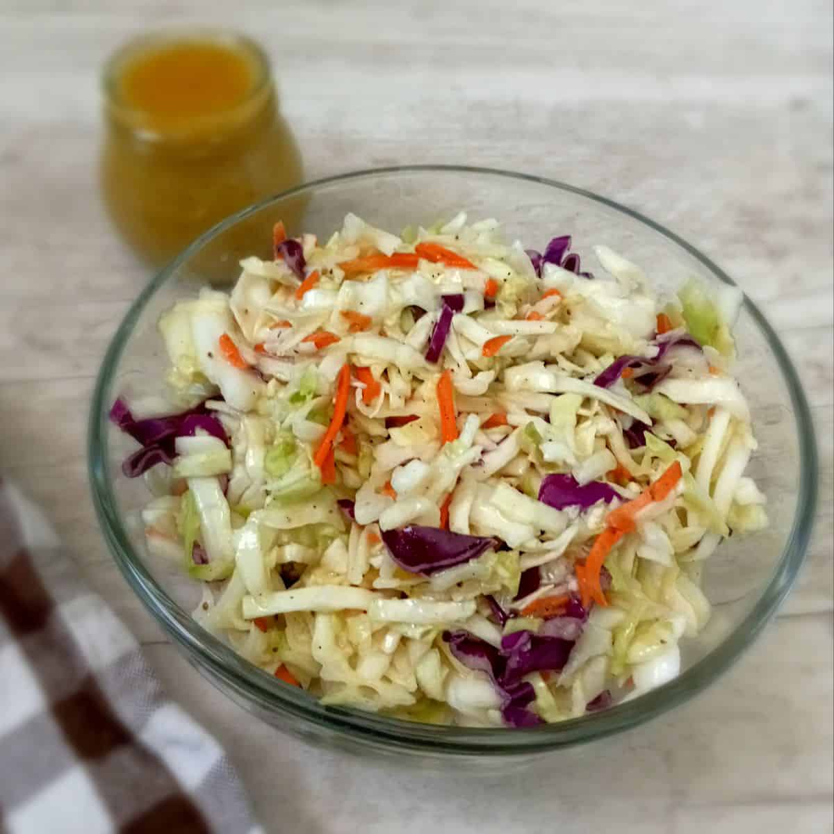 a glass bowl filled with Amish coleslaw and a bottle of dressing.