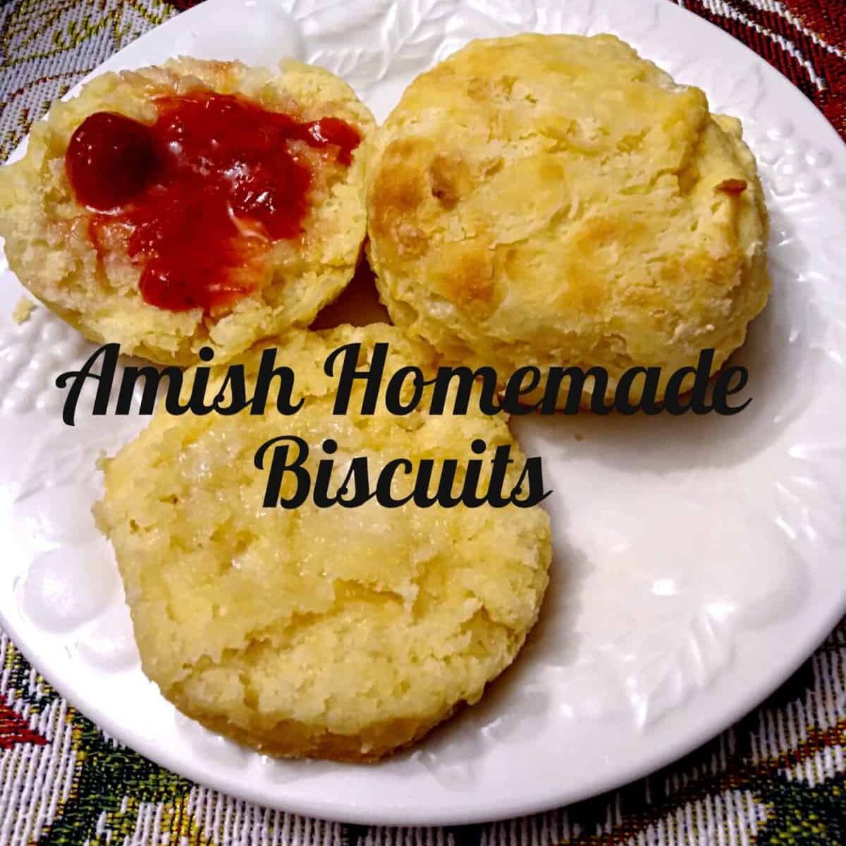 Amish buttermilk biscuits on a plate, one is cut in half and spread with butter and strawberry jam.
