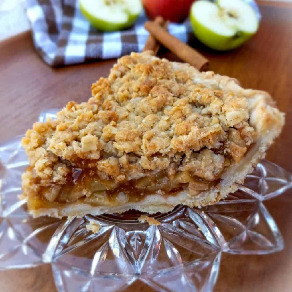 a slice of Dutch apple pie with crumb topping on a glass plate.
