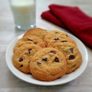 a plate of chocolate chip cookies with a cup of milk in the background.