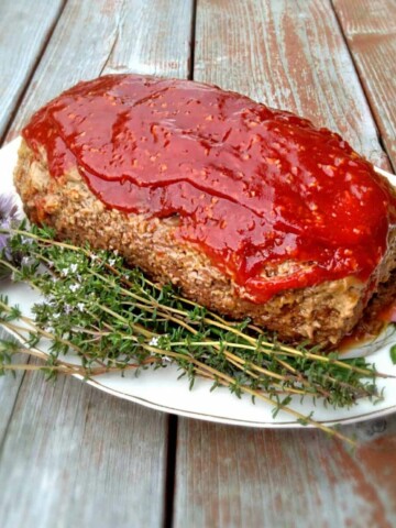 a whole meatloaf on a plate with fresh herbs.