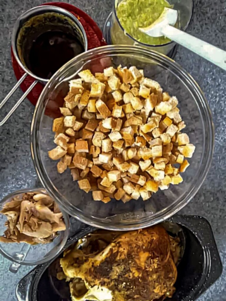 bread cubes in bowl, chopped veggies in chopper bowl, browned butter in saucepan, and cooked chicken in roaster.