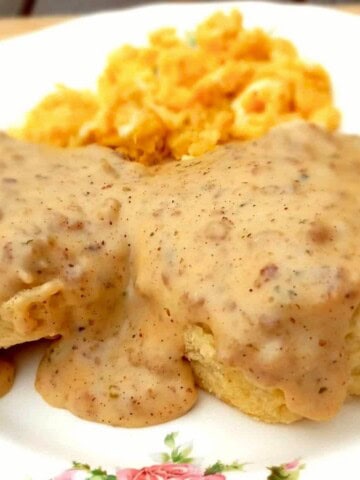 homemade sauage gravy over biscuits on a plate with scrambled eggs.