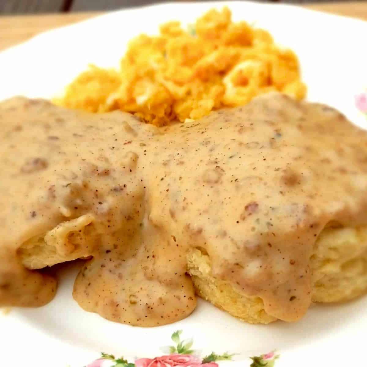 homemade sauage gravy over biscuits on a plate with scrambled eggs.