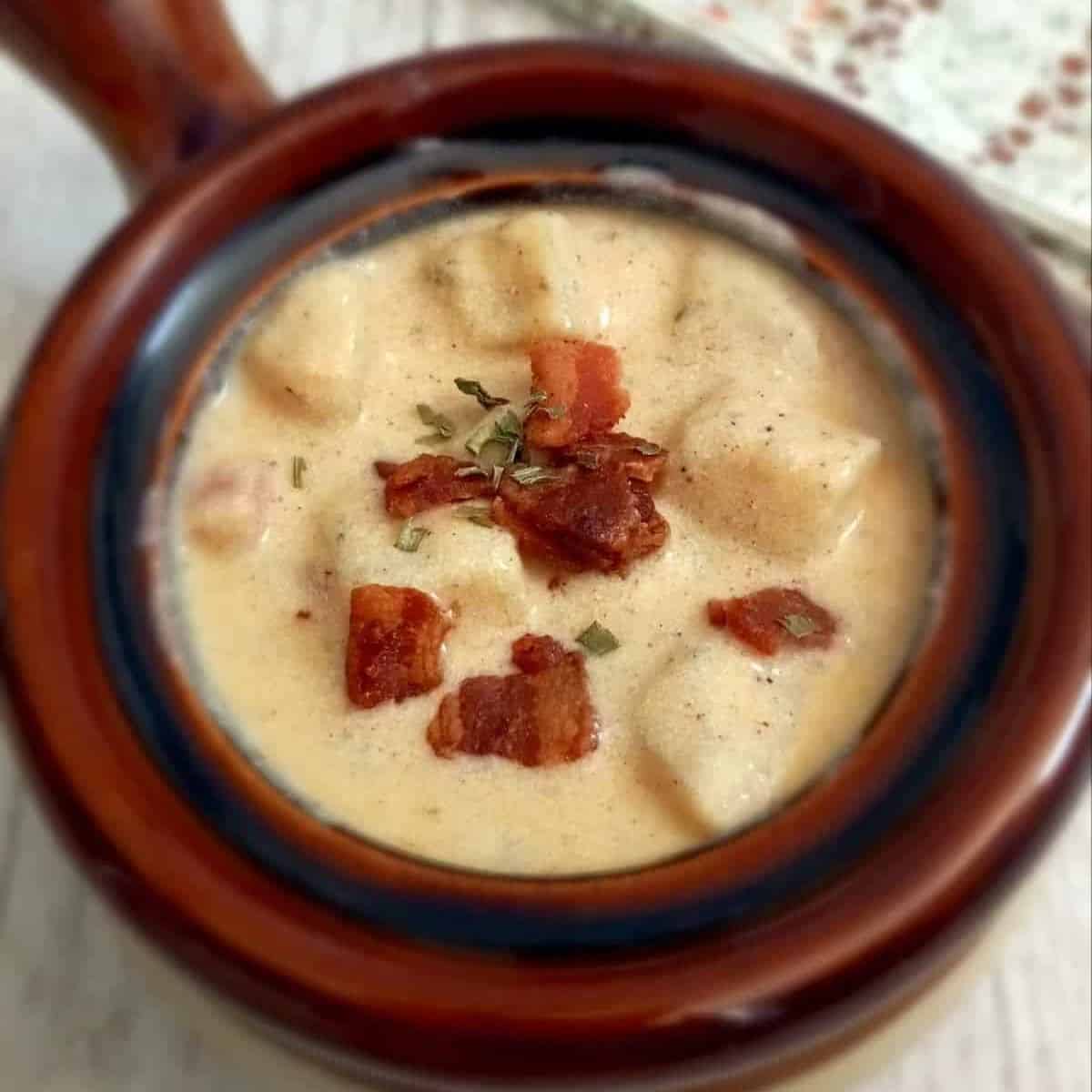 a small brown crock full of creamy potato soup topped with bacon pieces.