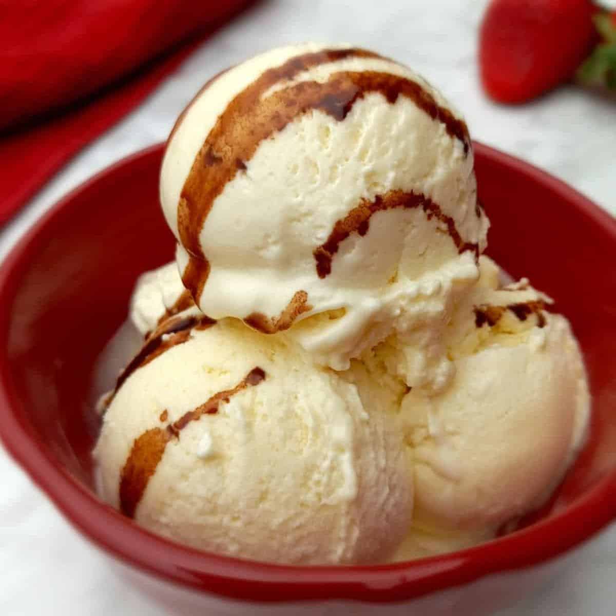 a red bowl with three scoops of homemade ice cream topped with chocolate syrup.
