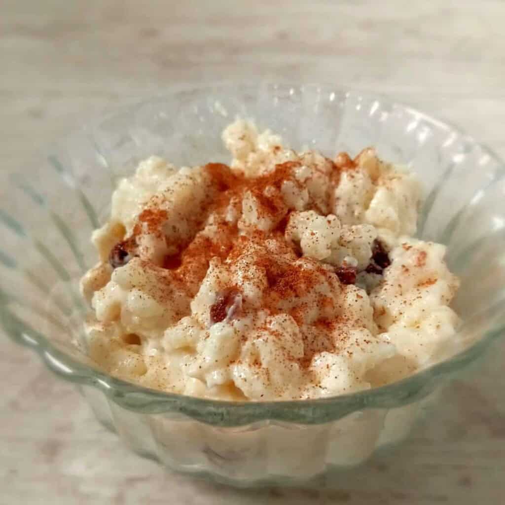 a glass bowl of raisin rice pudding sprinkled with cinnamon and nutmeg.