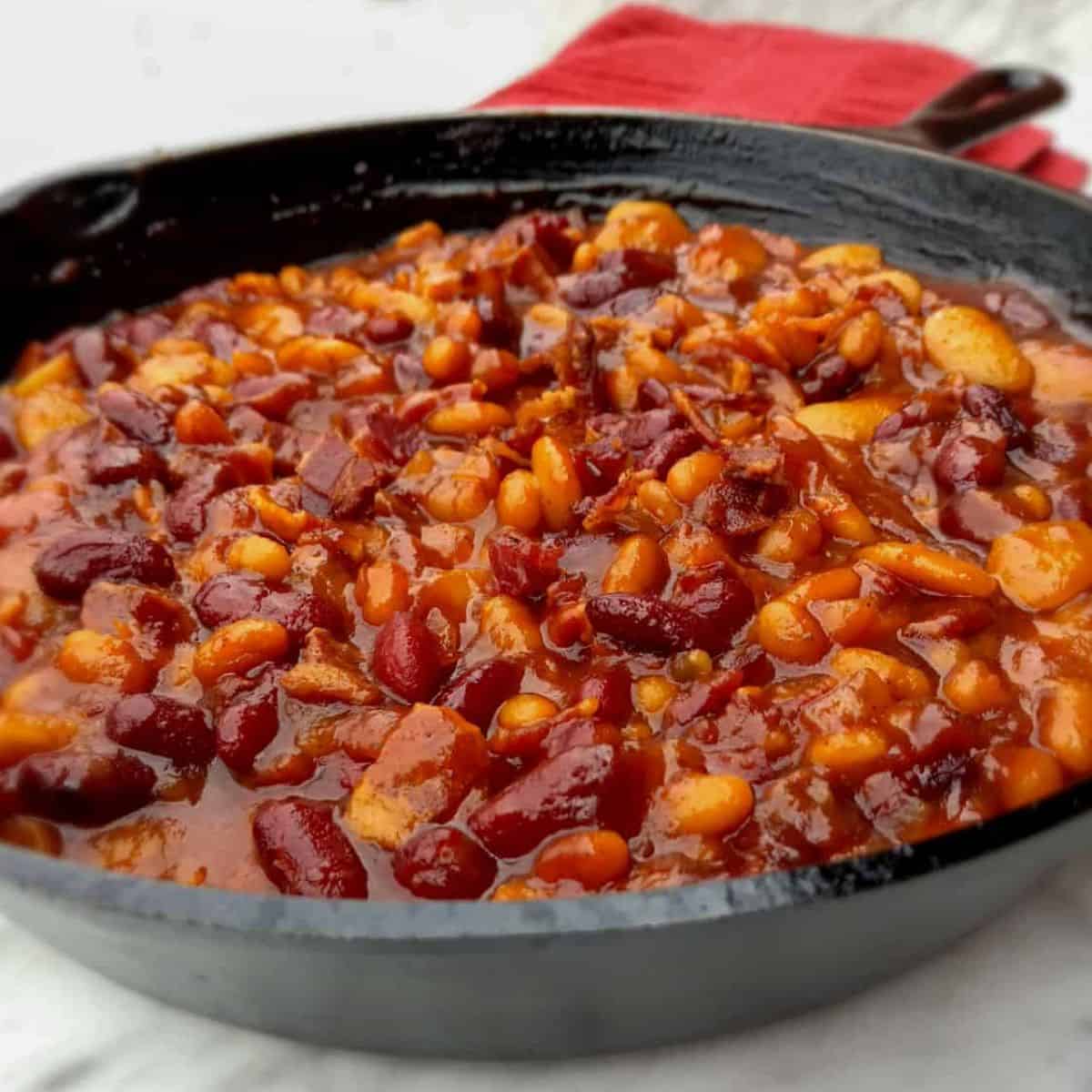 a cast iron skillet full of homemade baked beans with bacon and onion.
