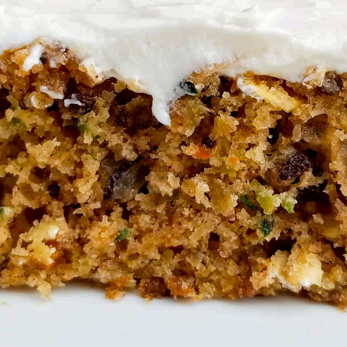 a close-up look at an Amish zucchini bar with shredded zucchini, shredded carrots, chopped nuts, and topped with cream cheese frosting.