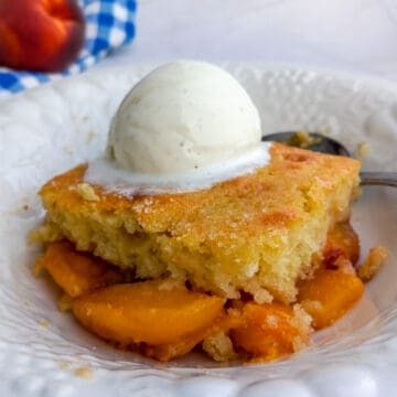 a slice of peach cobbler in a dish with a scoop of ice cream