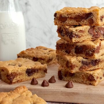 stack of chocolate chip bars on a board and a jar of milk in the background