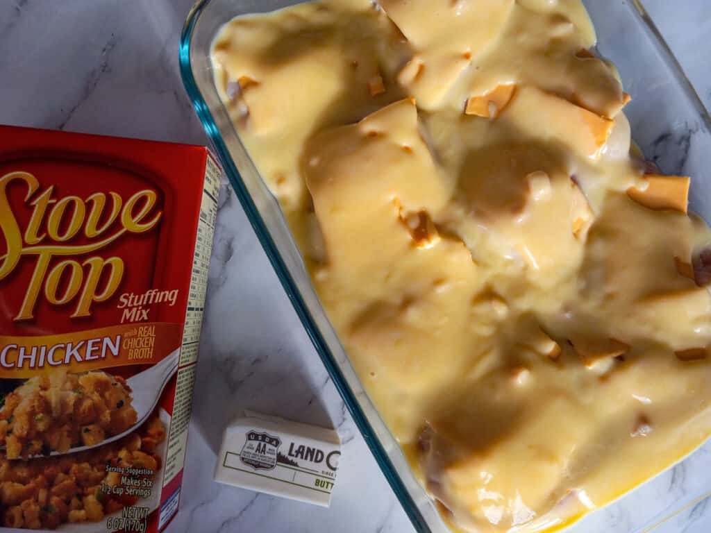 chicken in pan topped with cheese and cream soup, and a box of stovetop stuffing and butter
