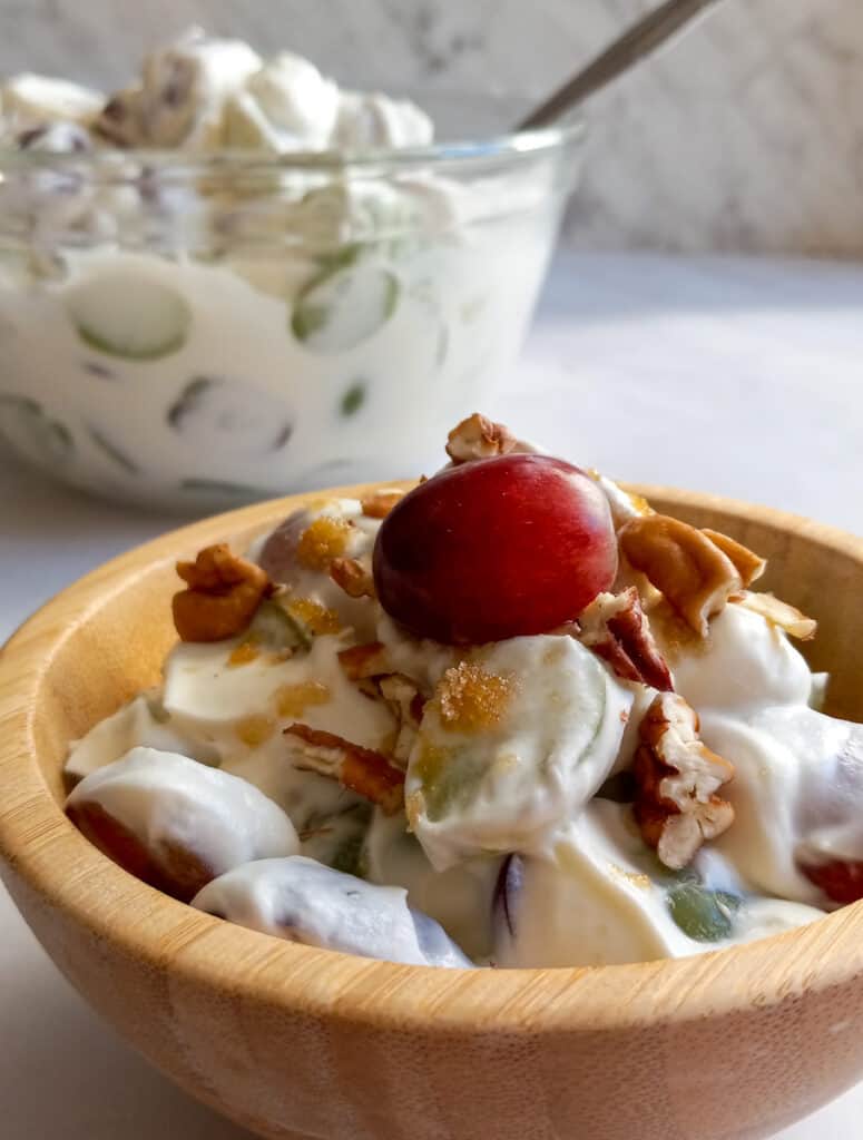 big bowl of grape salad and small wooden bowl full with pecans and brown sugar on top