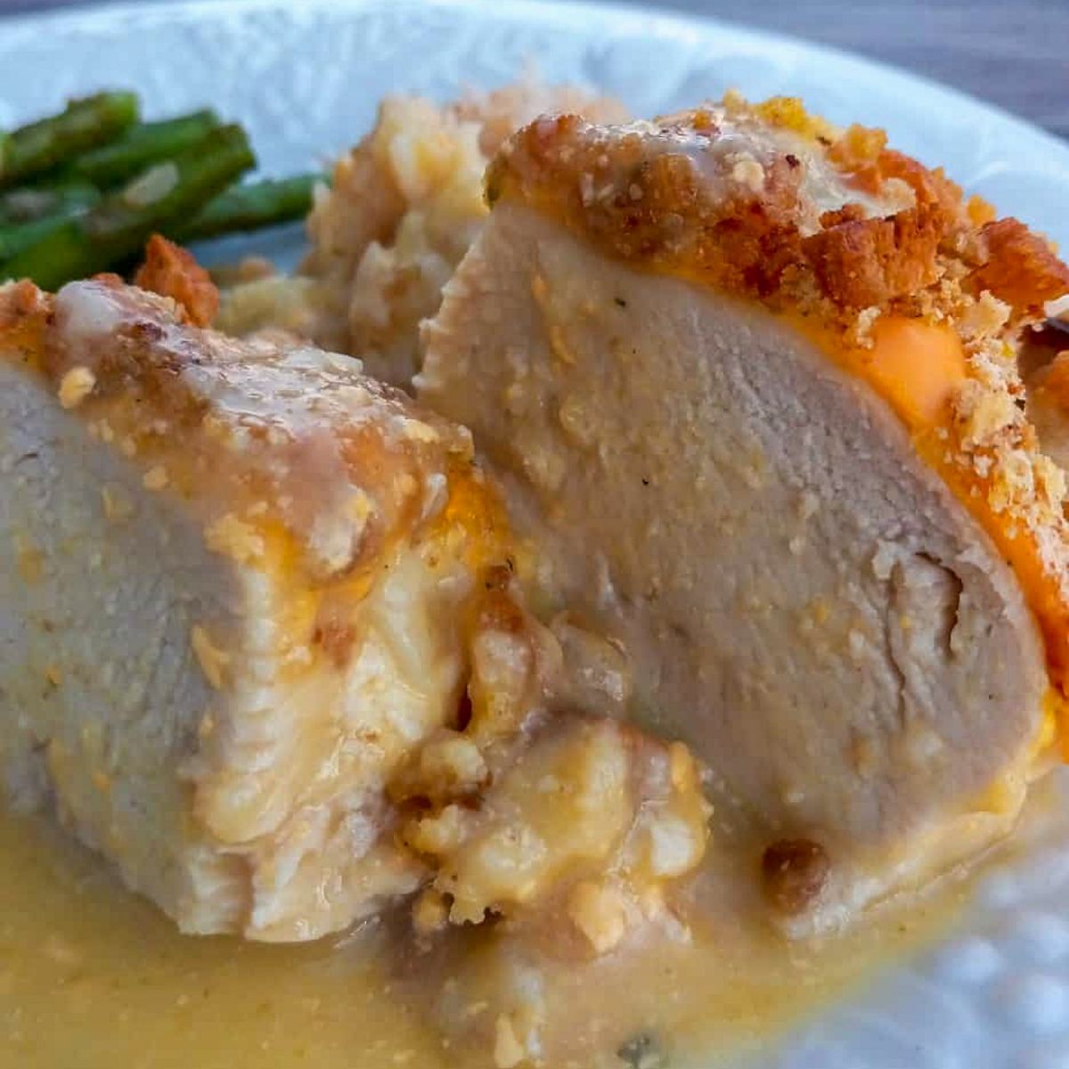cheese and stuffing topped oven-baked chicken breast on a plate with asparagus and scalloped potatoes.