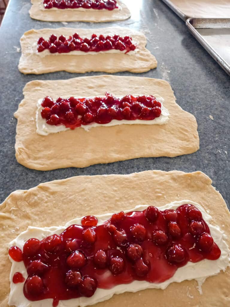cream cheese and cherry pie filling spread onto four danish pastry doughs