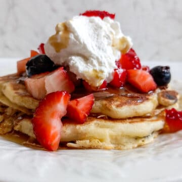 Amish pancakes topped with Nutella, berries, whipped cream, and maple syrup