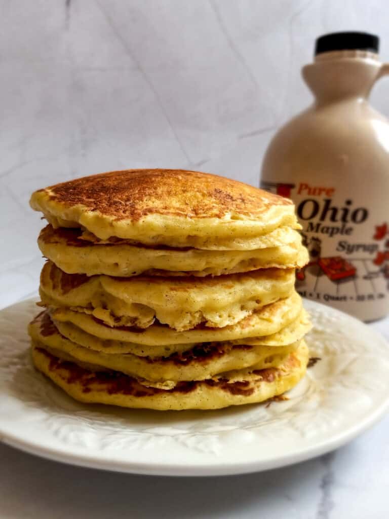stack of cooked pancakes and a jug of maple syrup