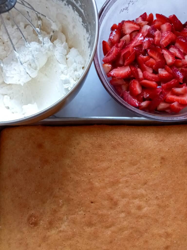 shortcake in 9x13", bowl of sliced strawberries, and a bowl of whipped cream