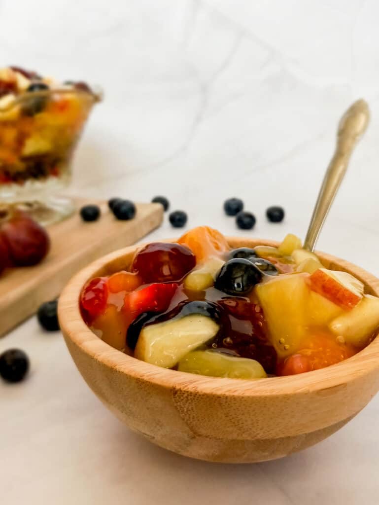 small bowl of fruit salad and larger glass dish with fruit salad and fruits scattered around