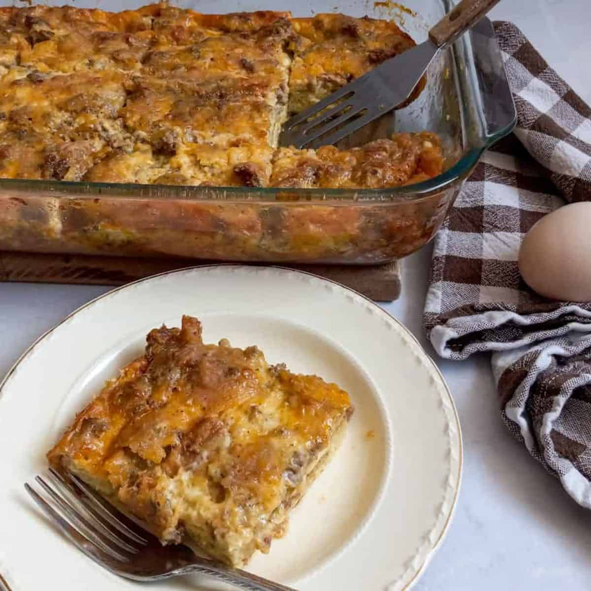 a slice of Amish breakfast casserole with bread on a plate, remaining pan in background.