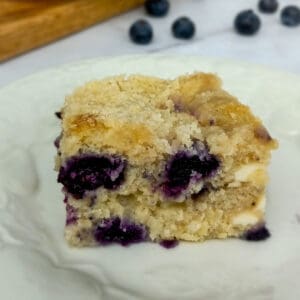 slice of Amish blueberry cream cheese coffeecake on a platter and blueberries scattered around
