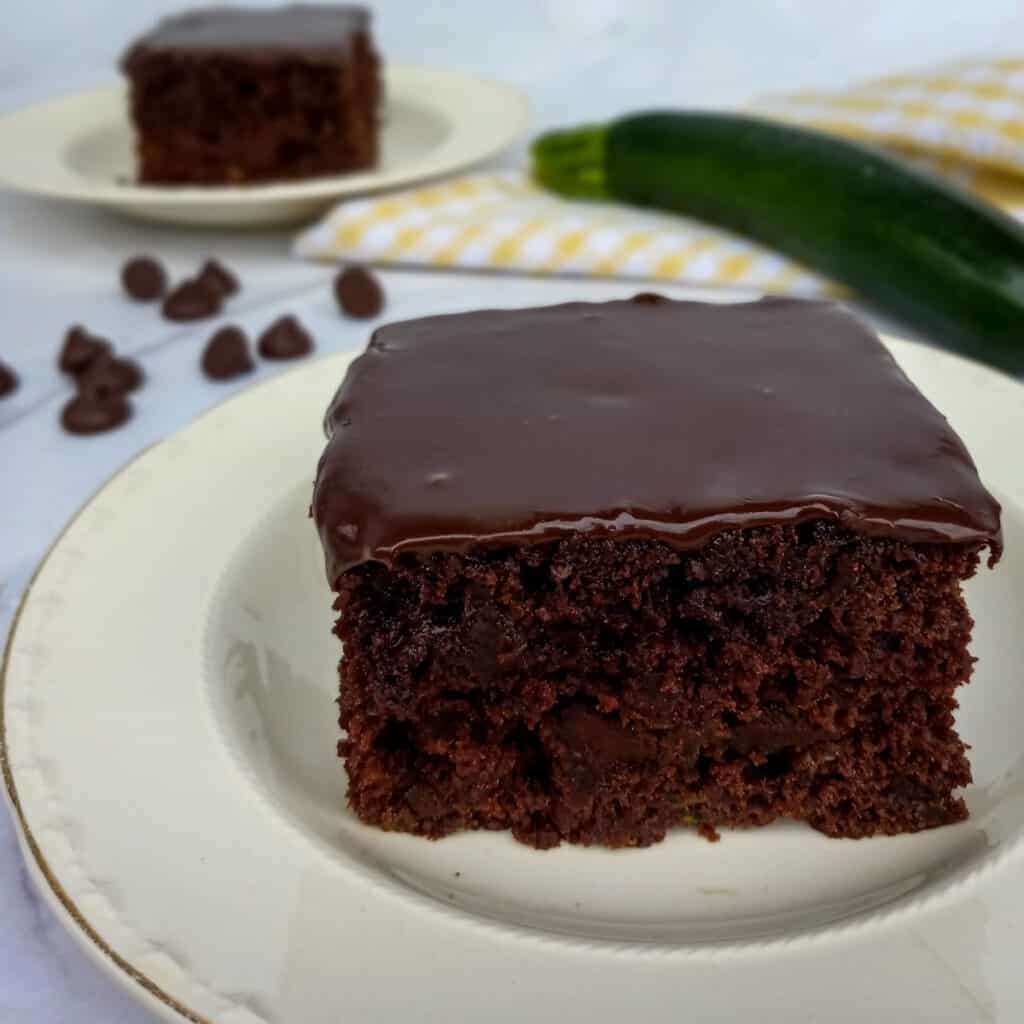 2 slices of Amish chocolate zucchini cake on plates, zucchini and towel in background
