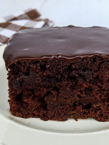 slice of fudgy zucchini cake on plate and a brown towel in background