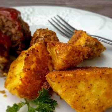 parmesan crusted potatoes on a plate with parsley and a mini meatloaf