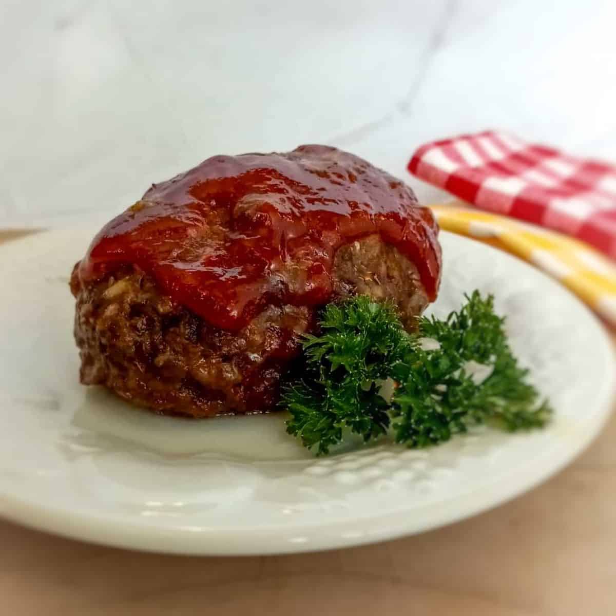 an Amish mini cheesy meatloaf on a plate with parsley and kitchen towels for decor