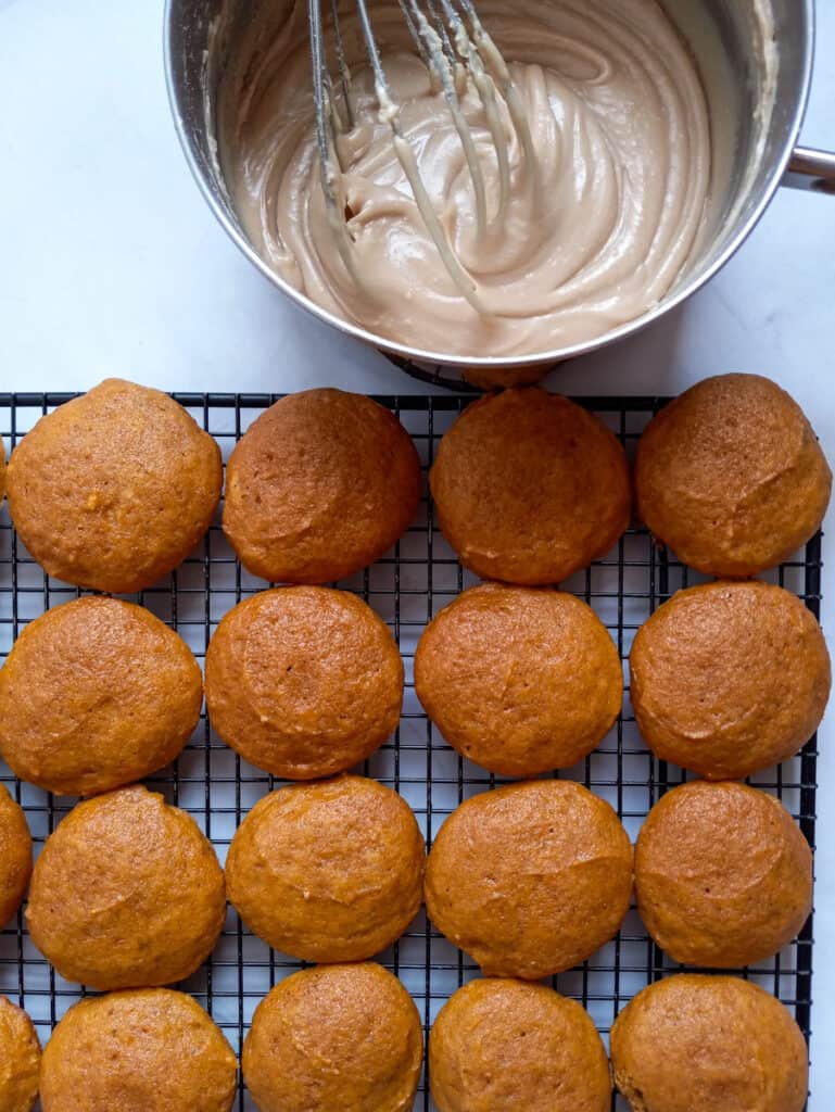 pumpkin cookies on a cooling rack and a bowl with caramel frosting