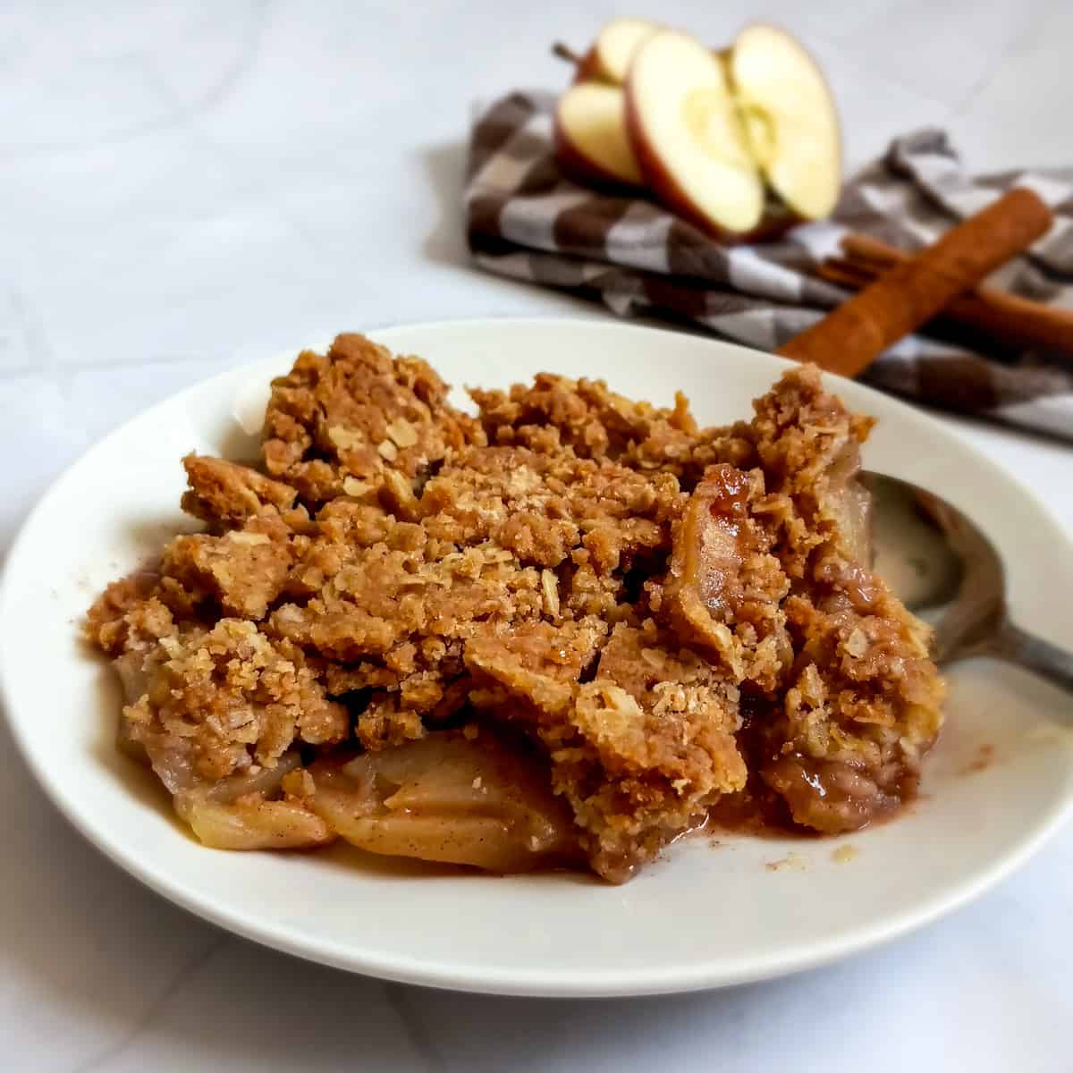 Amish apple crisp on a plate, apples and cinnamon sticks in the background