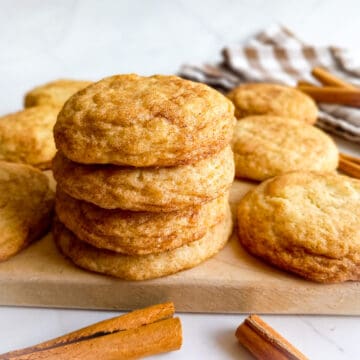 stack of Amish snickerdoodle cookies on a board and cinnamon sticks scattered around.