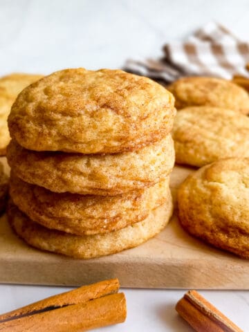 stack of Amish snickerdoodle cookies on a board and cinnamon sticks scattered around.