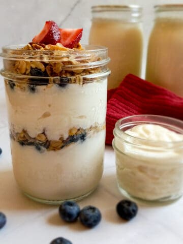 2 quart jars of vanilla yogurt, one tiny jar, and one pint jar filled with homemade vanilla yogurt, granola, and berries