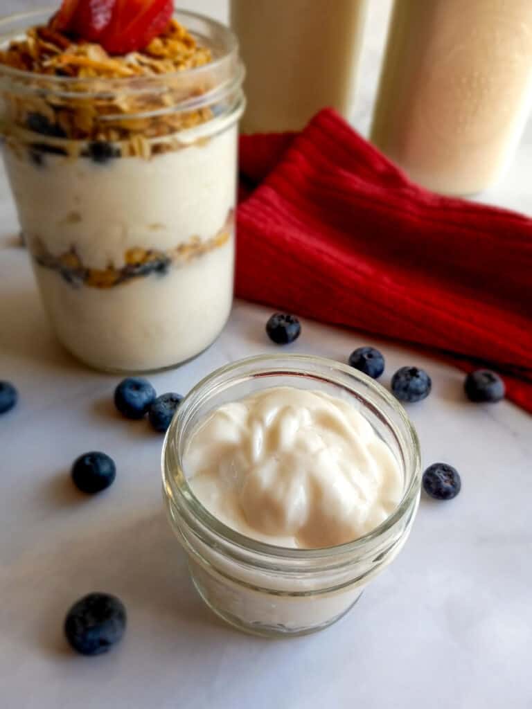 Amish yogurt in a small jar, a jar filled with yogurt parfait, and 2 quart jars.