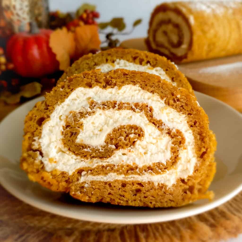 slices of Amish pumpkin roll on a plate and the rest of the roll in the background.