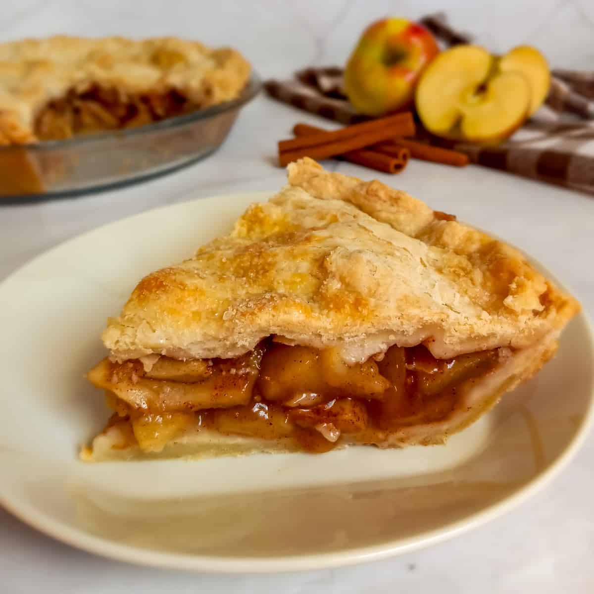slice of old-fashioned Amish apple pie on a small plate with a 9" pie in the background.