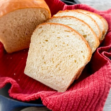 sliced homemade Amish bread in a skillet with a red towel along with part of a loaf.