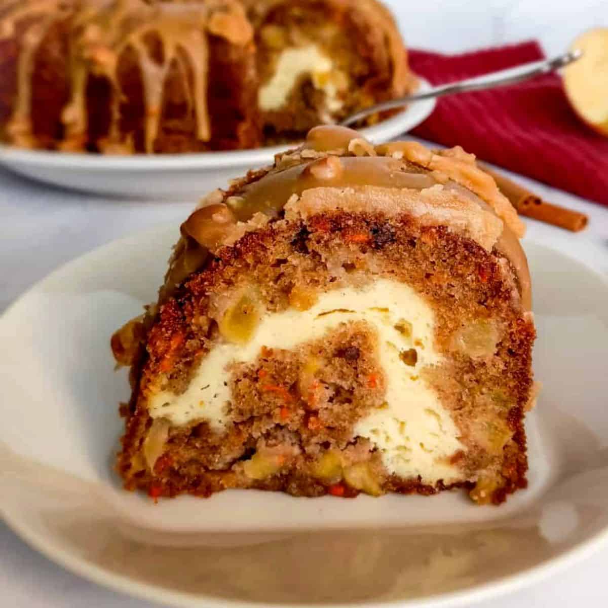 a slice of apple cream cheese bundt cake on a plate with the remaining cake in the background.