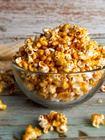 a glass bowl full of Amish caramel popcorn with a few pieces scattered around.