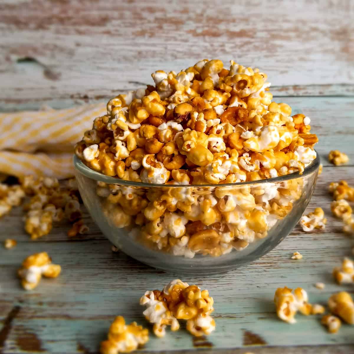 a glass bowl full of Amish caramel popcorn with a few pieces scattered around.
