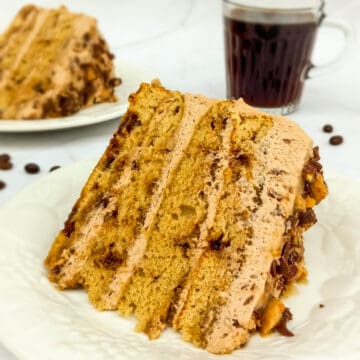 two slices of Layered Tiramisu torte cake on plates with a cup of coffee in the background.