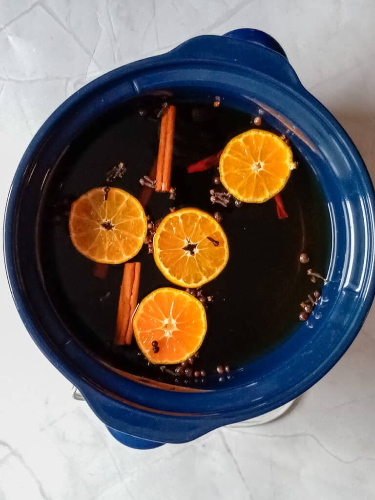 crockpot filled with apple juice, spices, and orange slices.