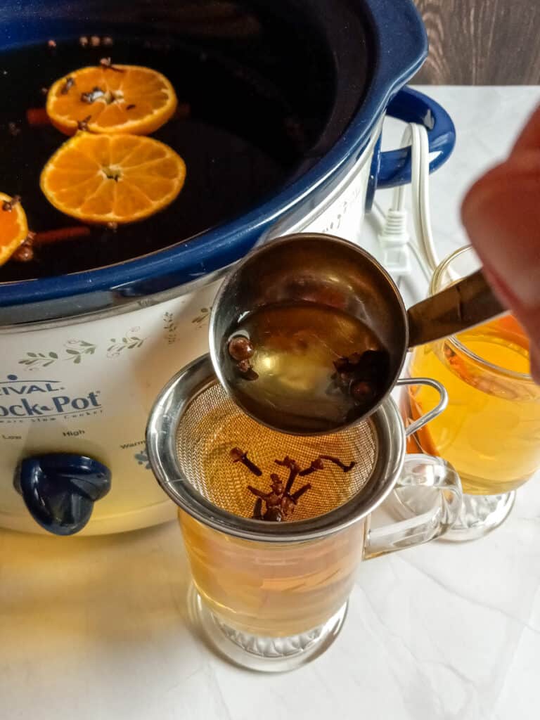 pouring cider into a cup through a strainer.