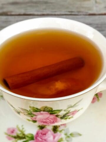 a beautiful rose mug of hot apple cider with a cinnamon stick.