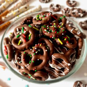 a bowl of almond bark coated pretzels topped with sprinkles and chocolate drizzle.
