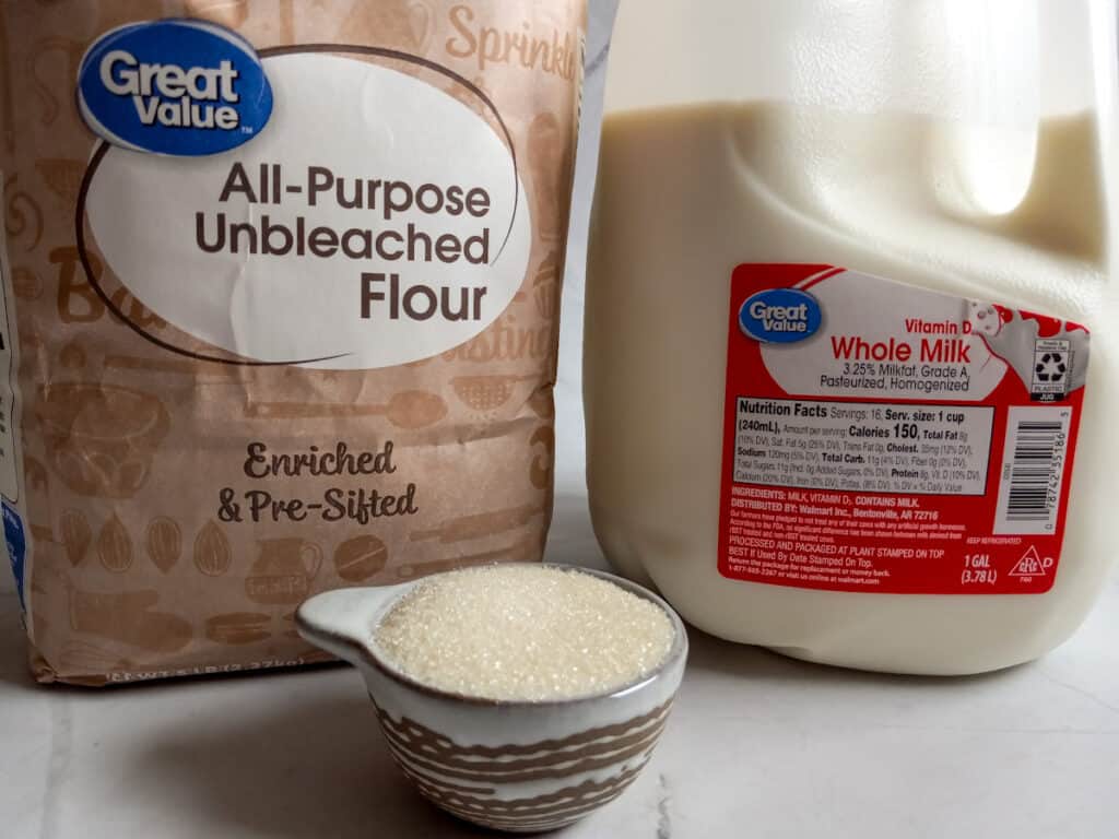 a jug of milk, bag of flour, and a cup with sugar.