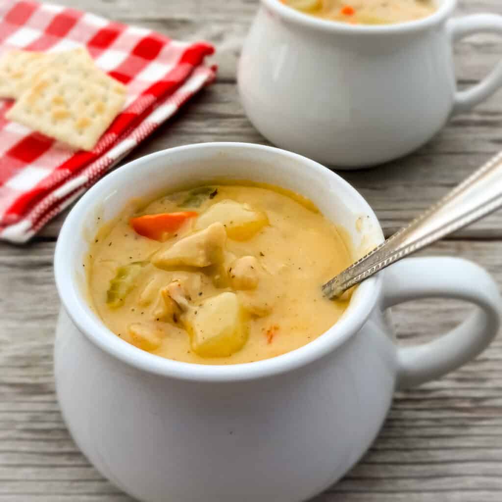 a small crock full of hearty Amish chicken chowder soup featuring chicken, potatoes, and veggies, another crock in the background.