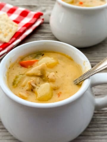 a small crock full of hearty Amish chicken chowder soup featuring chicken, potatoes, and veggies, another crock in the background.