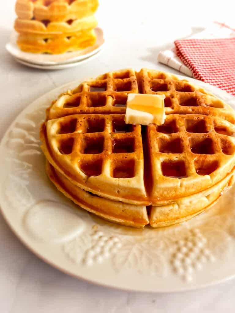 waffles stacked on a plate with butter and syrup on.